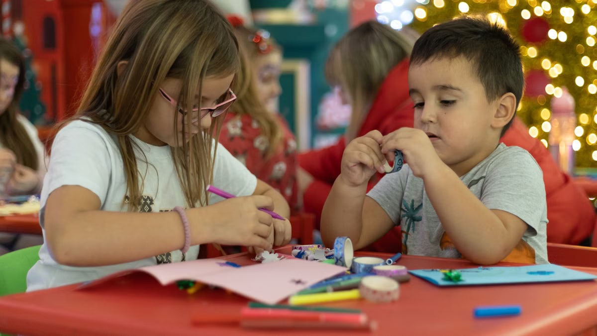 Two kids engaged in festive crafts at a decorated table, creating holiday ornaments.